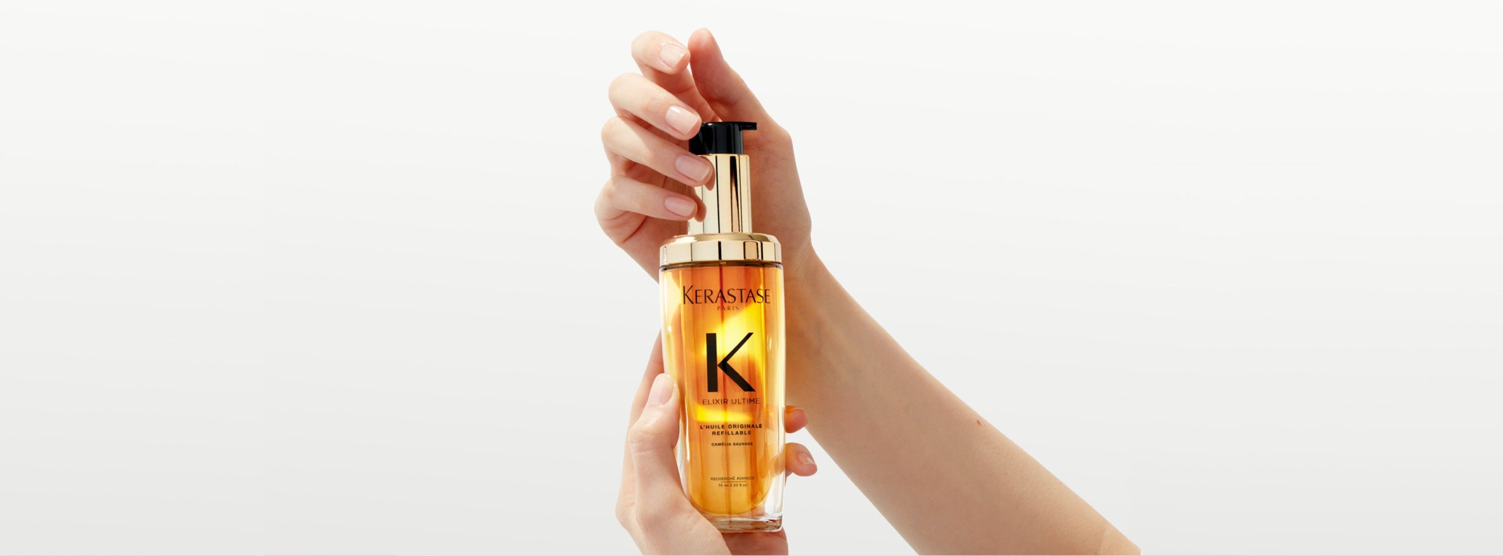 Novo Óleo Elixir Ultime com Refil O novo Elixir Ultime com refil está sendo segurado entre duas mãos em um movimento de torção.