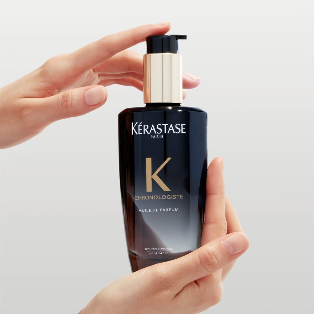 Óleo Capilar Chronologiste Fragrância Duradoura O óleo capilar Chronologiste Huile de Parfum, que apresenta uma mistura artística de fragrâncias cativantes que misturam cedro, magnólia e rosa-chá, está sendo segurado entre duas mãos.