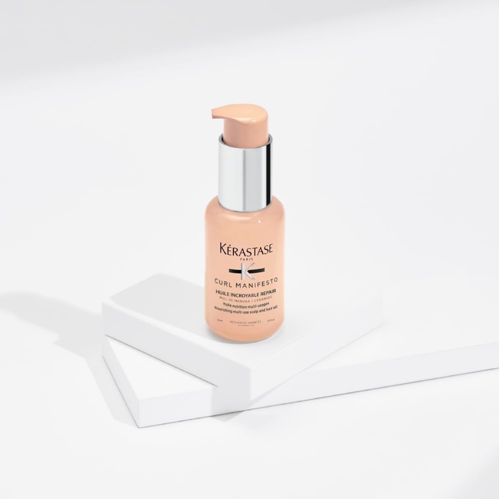 O óleo capilar Curl Manifesto Incroyable Repair é exibido em um fundo cinza puro com cubos transparentes. Esse óleo hidrata e define a forma dos cabelos cacheados, reduzindo o frizz e a quebra.